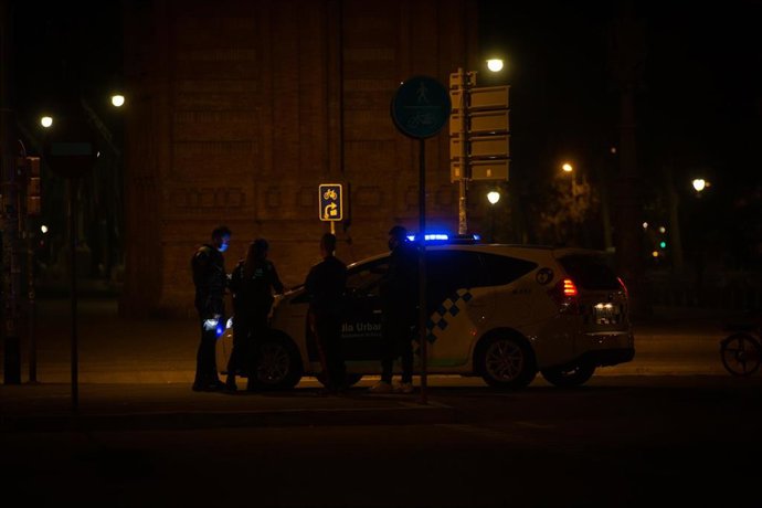 Un hombre firma en el capó de un vehículo de la Guardia Urbana una multa por saltarse el toque de queda.