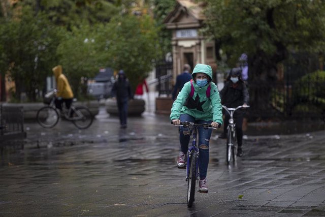 Varias personas circulan en bicicleta durante una jornada de lluvia en Sevilla