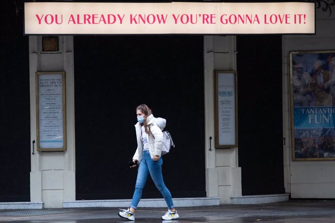 15 October 2020, England, London: A woman wearing a FACE mask walks beneath a sign outside theatre in Covent Garden. Photo: Dominic Lipinski/PA Wire/dpa
