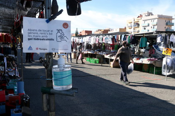 Pla tancat d'un cartell informatiu i de gel hidrolaclit i de fons un comprador caminant al mercat de Bonavista en el segon cap de setmana de confinament municipal. Imatge del 8 de novembre del 2020 (Horitzontal).