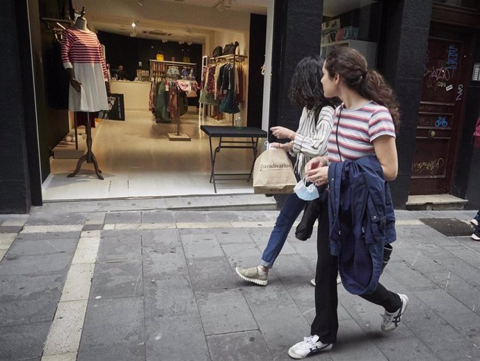 Dos jóvenes pasan por la puerta de una tienda de ropa en la jornada en la que Navarra inicia la Fase 2 de la desescalada instaurada por el Gobierno a consecuencia del coronavirus. En Pamplona, Navarra (España), a 25 de mayo de 2020.