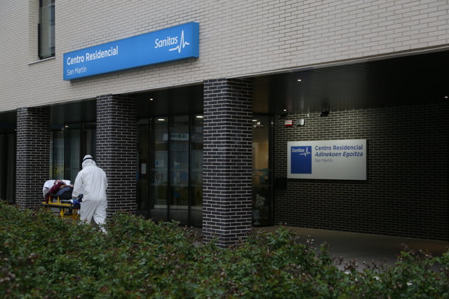 Un sanitario protegido con un traje, guantes y mascarilla, sale con una camilla de un centro sanitario en Vitoria