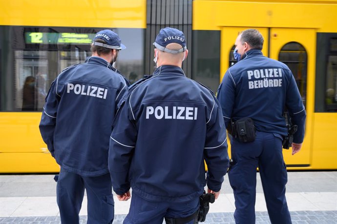 19 October 2020, Saxony, Dresden: (L-R) Policemen Andre Richter, Gabor Schulz, and Martin Mauthner stand in front of a tram at a stop on Postplatz as part of an operation to check the passengers' compliance with mask wearing obligations on public transp