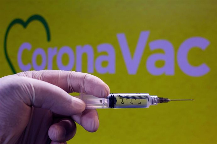 Jeringuilla frente al logotipo de CoronaVac, vacuna china contra el coronavirus