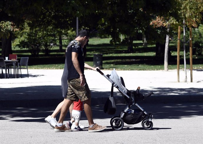 Una pareja y su bebé empujan el carrito en un parque de Madrid.