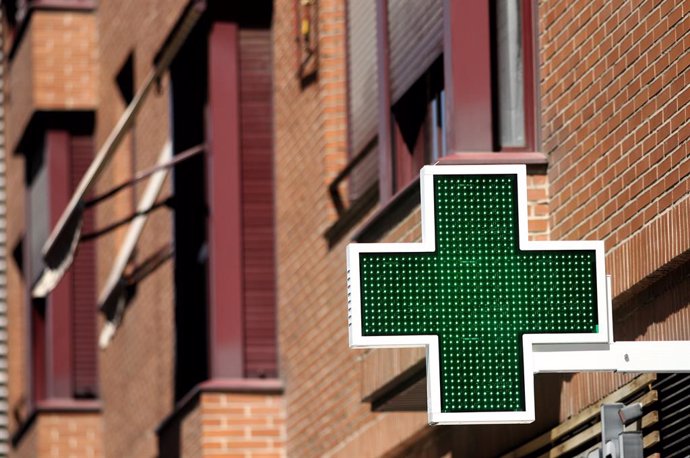 Una señal luminosa de la cruz verde a la entrada de una farmacia.