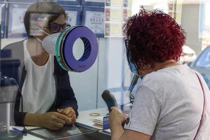 Una lotera de una dministración atiende a una clienta 