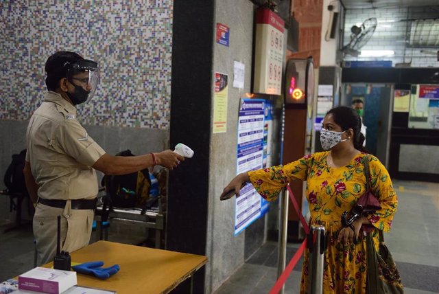 Un agente de la Policía de India toma la temperatura a una usuaria del metro de Calcuta antes de acceda a uno de los trenes.
