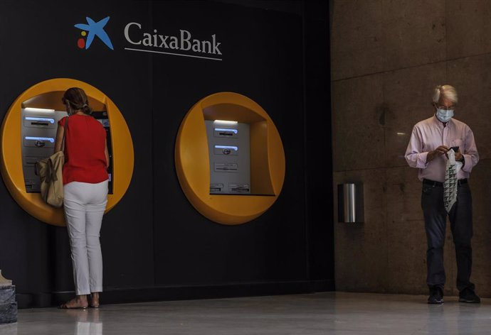 Dos personas en los cajeros dispuestos en el edificio de la sede de Caixabank, en Valencia.