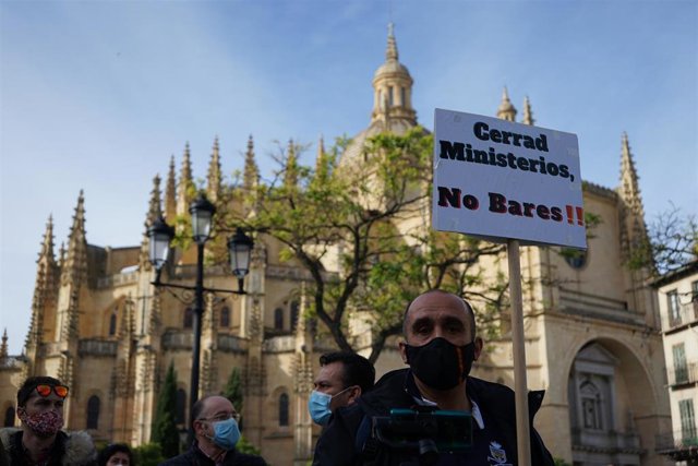 Uno de los manifestantes porta una pancarta contra el cierre de la hostelería con la Catedral de Segovia a su espalda.