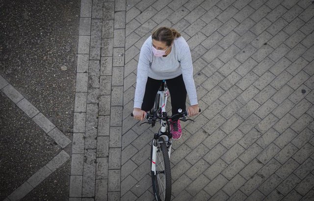 Una mujer en bicicleta, empleando una mascarilla.