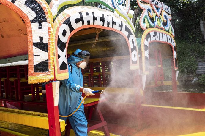 18 August 2020, Mexico, Mexico City: Aworker wearing a protective suit, disinfects the colorful boats (Trajineras) of Xochimilco, as the popular tourist spot prepare to reopen next Saturday, after months of closure due to the Coronavirus pandemic. Phot