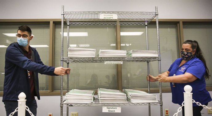 06 November 2020, US, Tampa: Ryan Bashore (L) and Lilly Rodriguez, employees of the Hillsborough County Supervisor of Elections office, bring in a collection of vote by mail ballots as they prepare to begin canvassing mail-in and provisional ballots dur