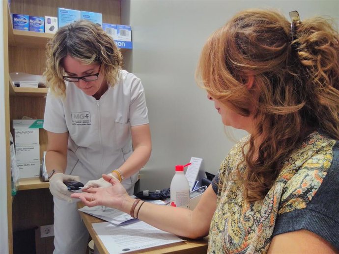 Una farmacéutica realiza una prueba de glucemia a una usuaria. Test diabetes