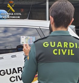 Un agente de la Guardia Civil sostiene un billete de 20 euros falso, con motivo de la investigación de tres jóvenes vigueses que introducían en el mercado este tipo de billetes, al hacer compras en establecimientos del sur de la provincia de Ponteareas.