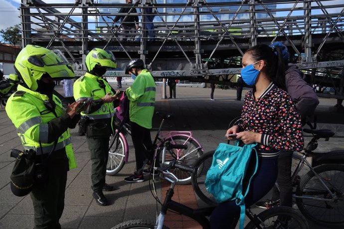 13 July 2020, Colombia, Bogota: Police officers check the documentation of a woman riding a bicycle while wearing a face mask amid strict lockdown restrictions to prevent the spreading of coronavirus. Photo: Camila Díaz/colprensa/dpa