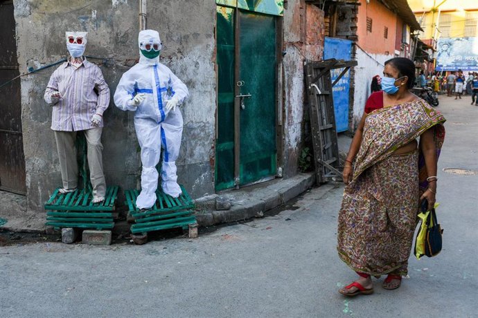 Una mujer camina frente a muestras de trajes protectores en plena pandemia del coronavirus en India.
