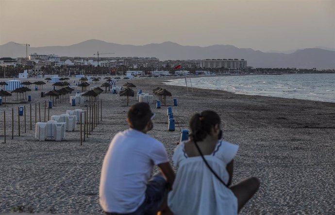 Dos jóvenes sentados contemplan la playa de la Malvarrosa de Valncia