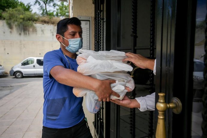 Una persona con mascarilla realiza una entrega a domicilio de alimentos en un programa solidario.