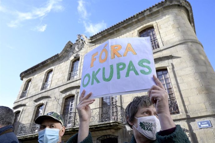 Una persona sostiene un cartel donde se puede leer "Fuera okupas" durante una marcha cívica para pedir la devolución de la Casa Cornide