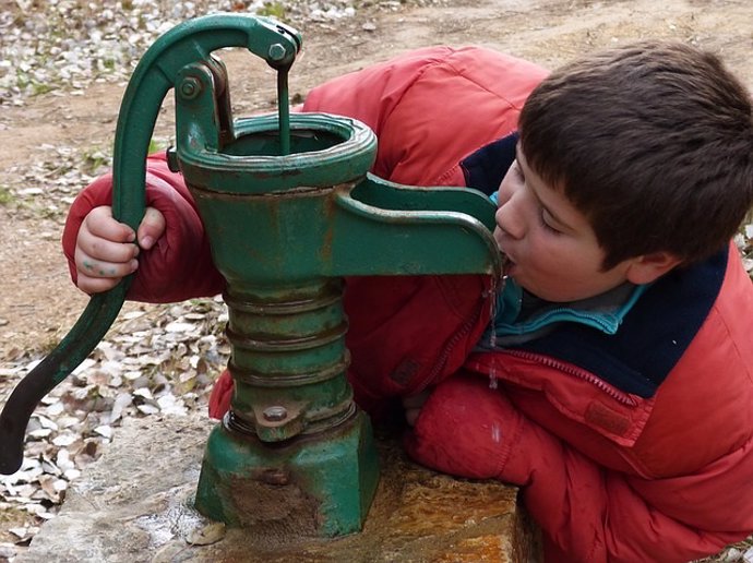 Niño bebe agua de una fuente.