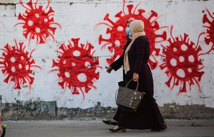 Mujeres junto a un mural sobre el coronavirus en el campamento de refugiados de Nuseirat, en la Franja de Gaza