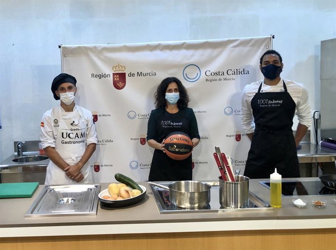 La consejera de Turismo, Cristina Sánchez, en el centro, junto al capitán del equipo de baloncesto Ucam Murcia CB, Sadiel Rojas, en una demostración culinaria para promocionar la marca 'Región de Murcia-Costa Cálida'