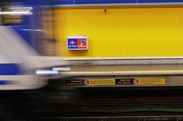 Un tren entra en una estación en la que se ve uno de los carteles que la Comunidad de Madrid ha instalado a lo largo del borde del andén en las estaciones del Metro de Madrid para que puedan ser vistas desde enfrente, y que se han colocado además en los b