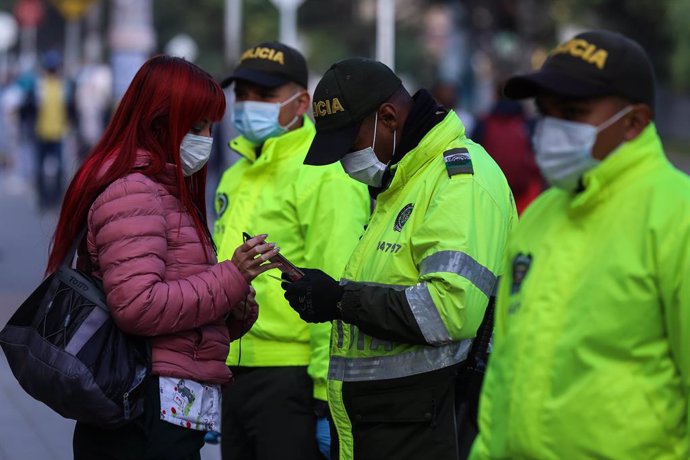 03 April 2020, Colombia, Soacha: A security officer wearing a face mask looks at the permit of a woman during the quarantine decree in the country to prevent the spread of the coronavirus. Photo: Camila Diaz/colprensa/dpa