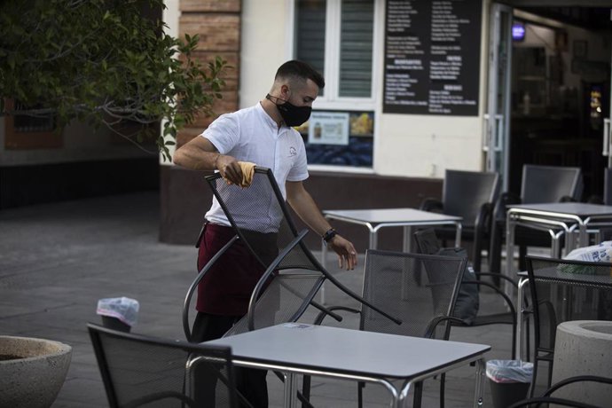 Un camarero recoge el mobiliario de la terraza de un bar, tras la nueva medida de restricción que obliga al cierre de toda actividad no esencial a partir de las 18 horas en Sevilla