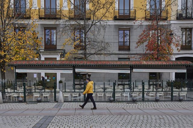 Una persona pasea al lado de una mampara instalada en un restaurante de la Plaza de Oriente, en Madrid (España), a 12 de noviembre de 2020.