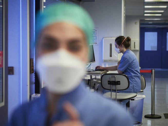 Una enfermera protegida con mascarilla mira a la cámara mientras otra empleada trabaja con el ordenador en las instalaciones pertenecientes a la UCI de la Clínica Universidad de Navarra, en Pamplona, Navarra, (España).