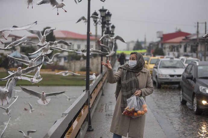 Una mujer con mascarilla alimenta a unos pájaros en Tonekabon, Irán