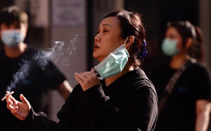 Una mujer se retira la mascarilla para fumar en Hong Kong.