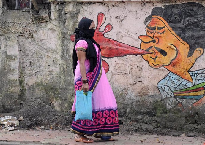 Una mujer con mascarilla pasea frente a un mural que recuerda los riesgos de contagio del coronavirus en India.
