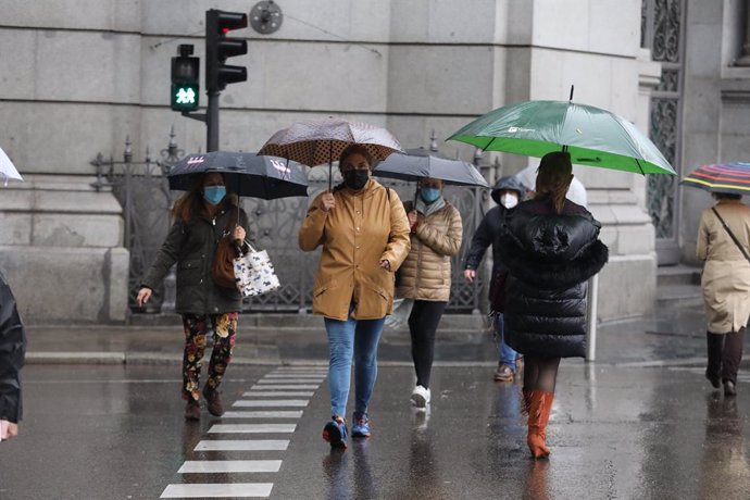 Transeúntes caminan por el centro de la capital protegiéndose de la lluvia con paraguas, en Madrid (España).