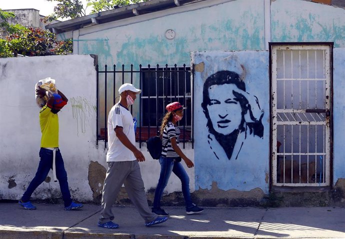 Personas con mascarillas ante un mural de Hugo Chávez en Carabobo