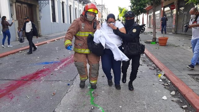 Una mujer afectada por el gas lacrimógeno y un policía durante las protestas contra el presidente Alejandro Giammattei en Guatemala