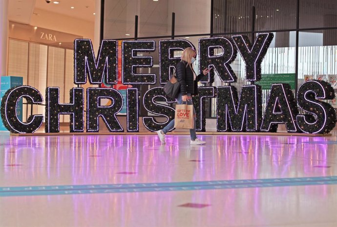 24 November 2020, England, London: A woman walks past Christmassy decorated letters made of fir branches, which are installed in a shopping centre and form the words "Merry Christmas". Photo: Yui Mok/PA Wire/dpa