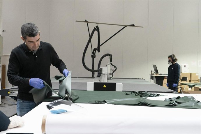 Dos operarios, uno de ellos protegido con una máscara, manejan material en la empresa 