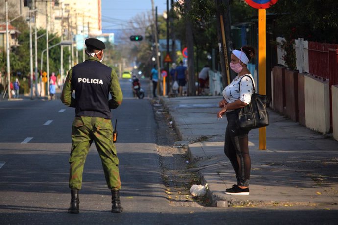 04 April 2020, Cuba, Havana: A policeman wears a face mask as he stands next to a woman in a deserted street in the El Carmelo district. Cuba has sealed off a part of downtown Havana popular with tourists because of the Coronavirus pandemic. Photo: Guil