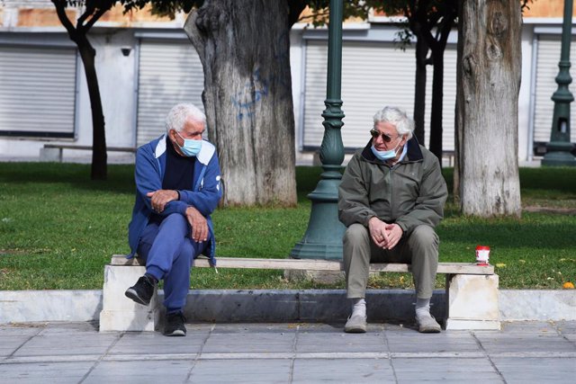 Dos hombres con mascarilla dialogan en un parque de Atenas