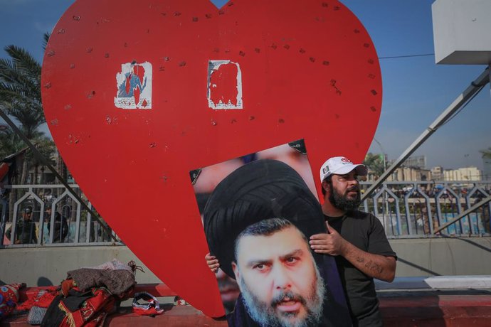 27 November 2020, Iraq, Baghdad: A supporter of Iraqi Shia cleric Muqtada al-Sadr holds his photo as he takes part in a rally in support of him at Tahrir Square. Al-Sadr called on Friday the masses of the Sadrist Movement to achieve a large majority in 