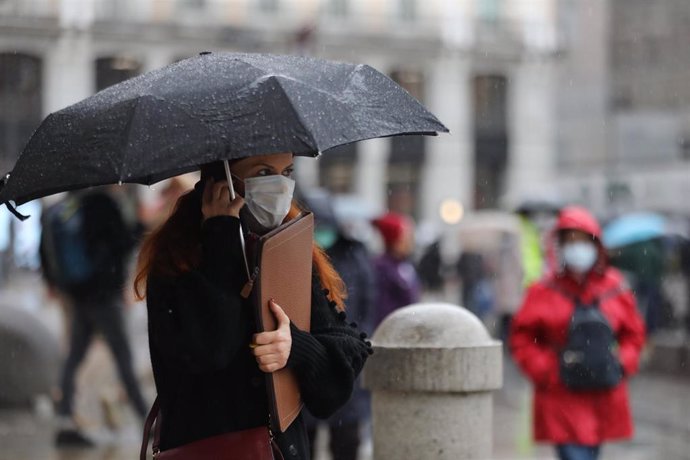 Una mujer pasea protegida con un paraguas por el centro de la capital, en Madrid