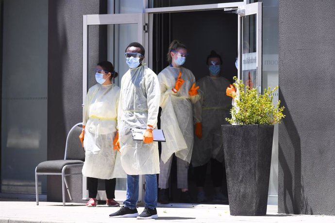 Trabajadores con equipos de protección esperan a la llegada de viajeros australianos que tendrán que pasar la cuarentena en un hotel de Canberra