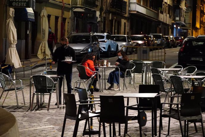 Un camarero trabaja en la terraza de un bar donde tres chicas consumen unas bebidas en Salamanca, la noche en la que la ciudad ha vivido su primer toque de queda dictado por la Junta de Castilla y León para toda la región, en Salamanca, Castilla y León 