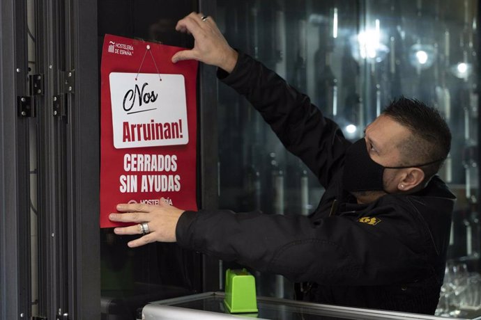 Un trabajador de hostelería coloca un cartel donde se lee "Nos arruinan. Cerrados sin ayudas", durante el primer día de reapertura de la hostelería en Logroño (España).