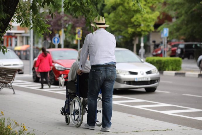 Un hombre pasea a una persona de edad avanzada en silla de ruedas.
