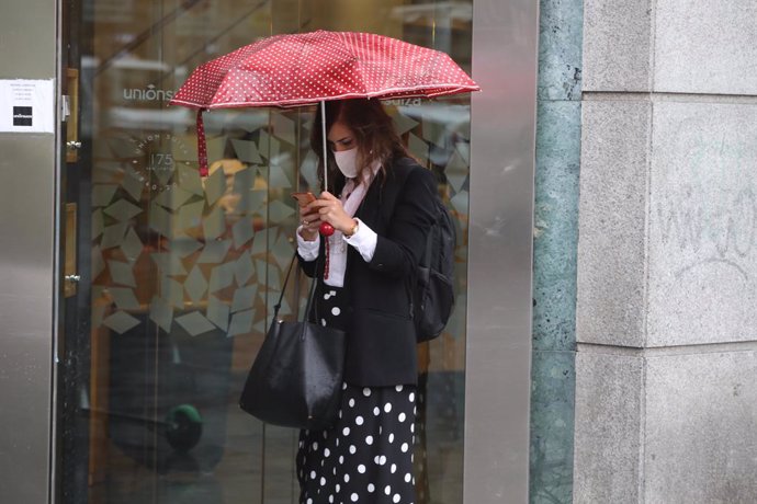 Una mujer protegida con un paraguas camina por el centro de la capital, en Madrid (España).