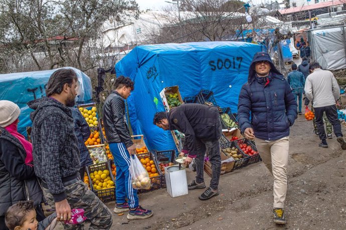 27 February 2020, Greece, Lesbos: A migrant buys fruit and vegetables at a stand in a temporary tent camp near the camp for migrants in Moria. Following serious clashes between police and angry inhabitants of the Greek island of Lesbos, which left dozen